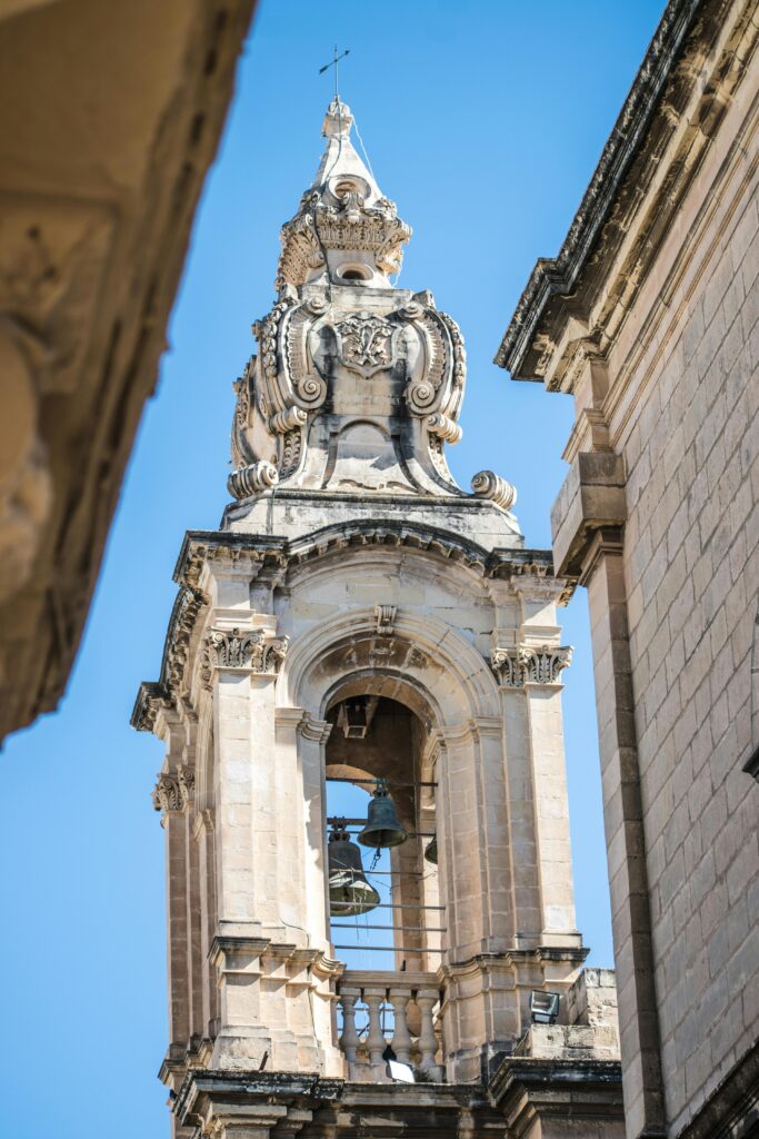 pexels-photo-12280220-12280220 A detailed view of a historic Baroque bell tower with intricate carvings and a clear blue sky backdrop.
